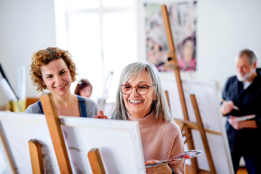 Mature woman smiling and painting with instructor in group class