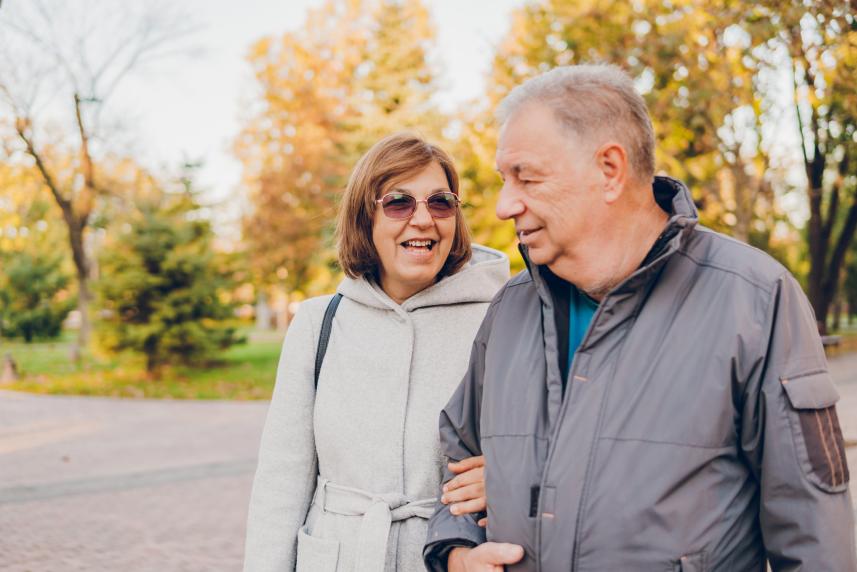 A couple walks arm in arm down a road in autumn.