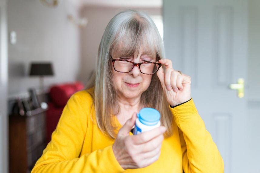 An older woman in a yellow sweater reads her prescription bottle