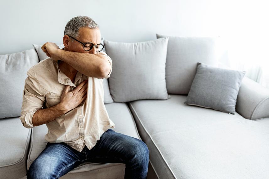 Man sitting on sofa coughing into arm