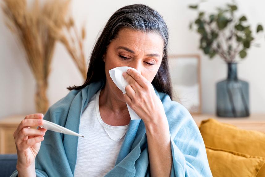 Mature woman blowing nose and looking at thermometer