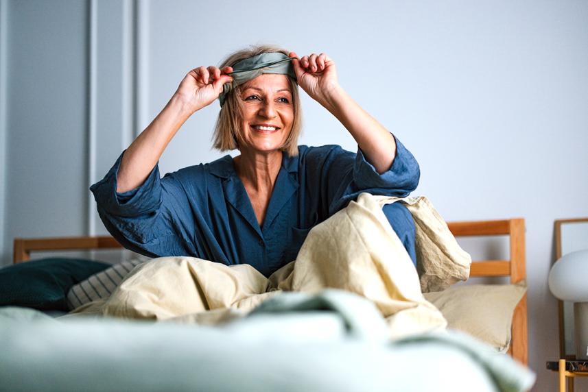 Mature woman smiling, waking up in bed and taking off sleep mask