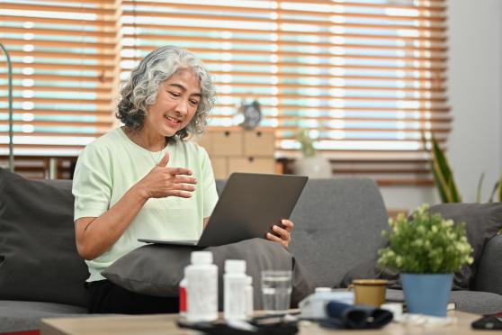 An older woman in a light green shirt rests a laptop in her lap