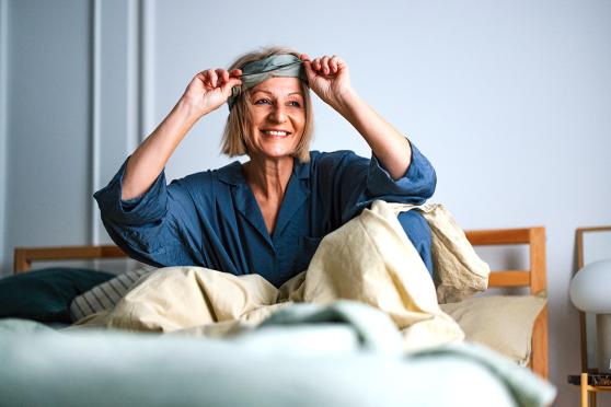 Mature woman smiling, waking up in bed and taking off sleep mask