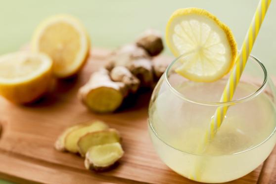Pitcher with lemonade and yellow straw on a cutting board with a piece of raw ginger and a lemon cut in half